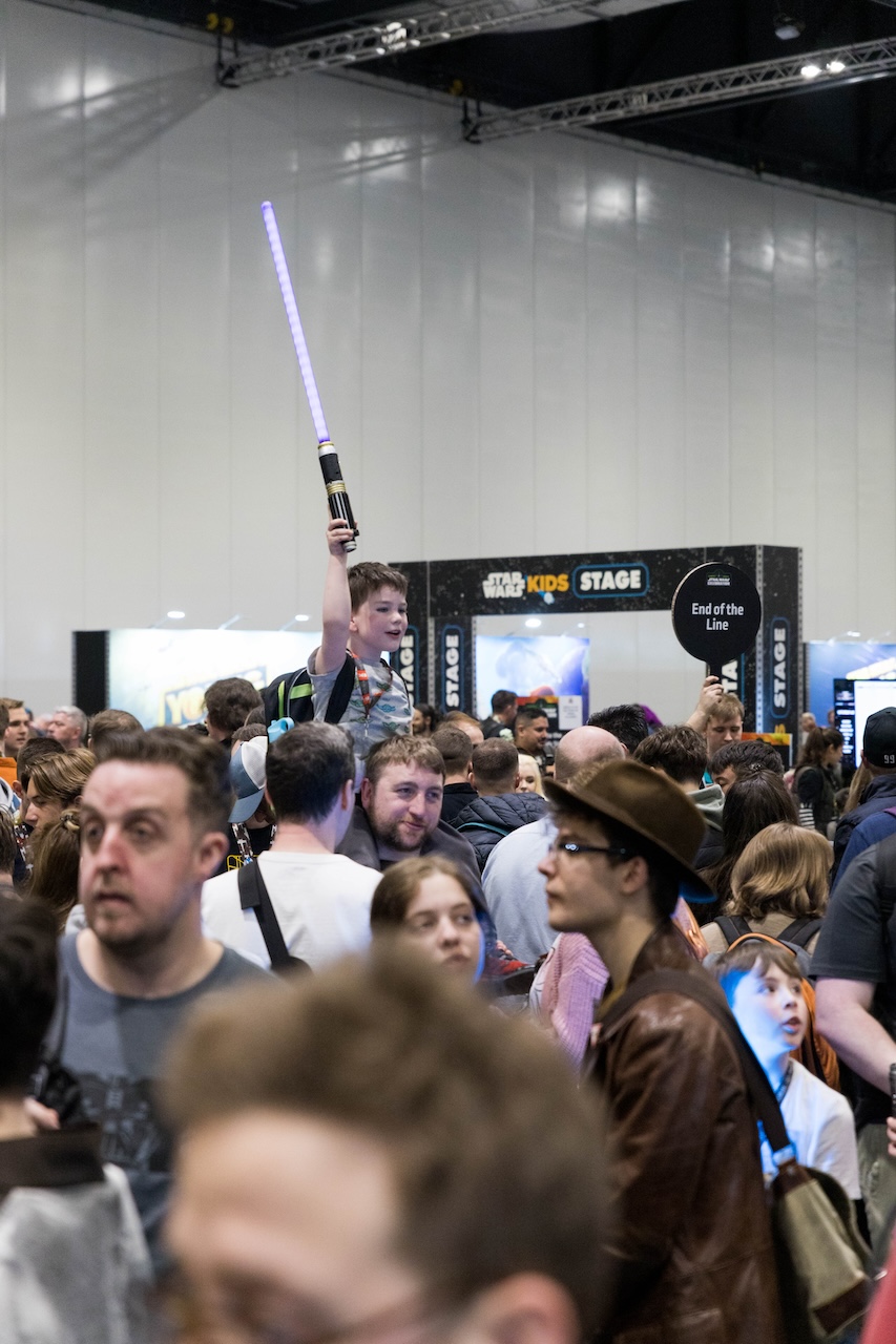 A boy in the crowd raises a lightsaber